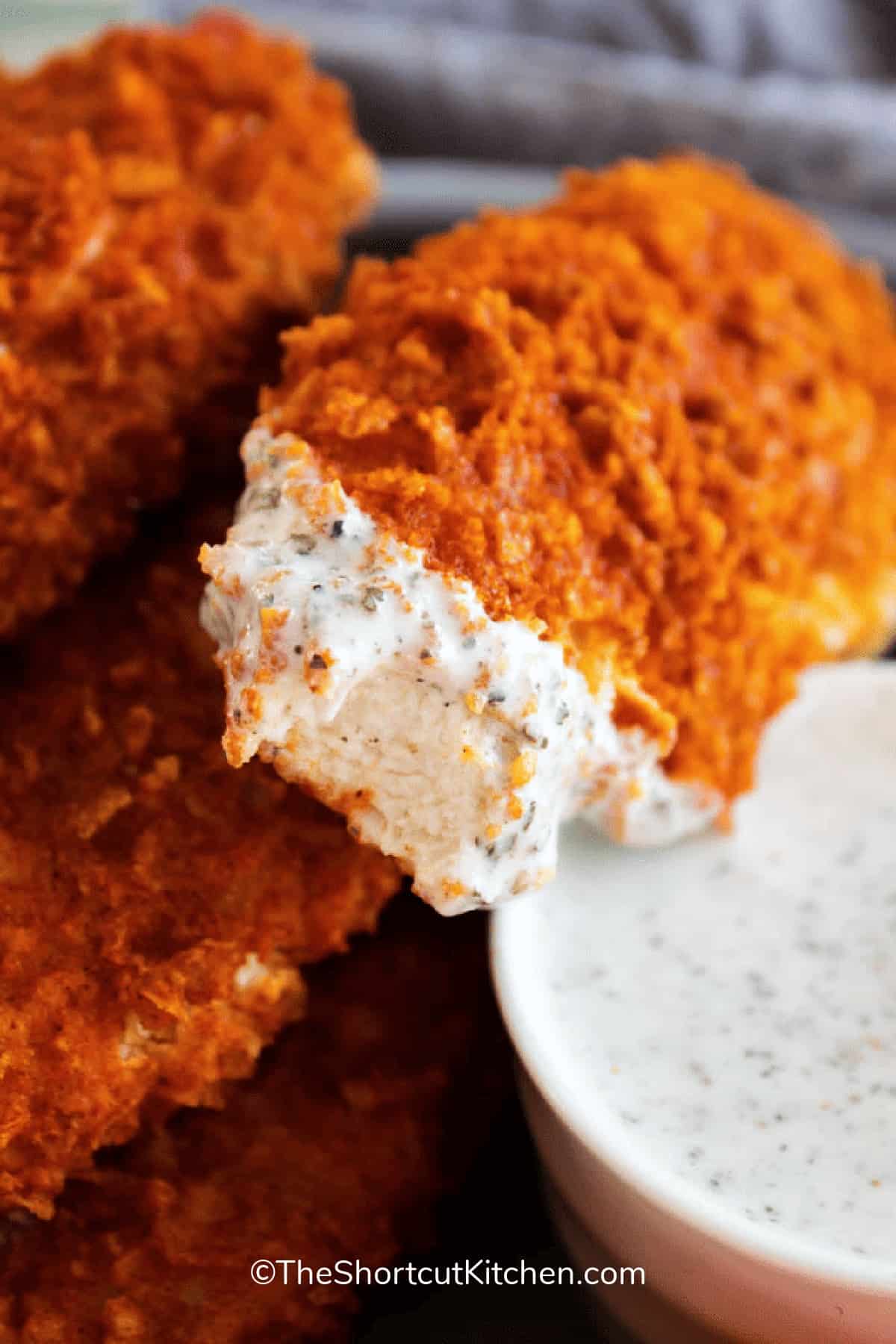 Crispy buffalo chicken tenders piled together, one with a bite taken out of it.