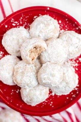cropped snowball cookies on a red plate with a bite taken out of one of the cookies