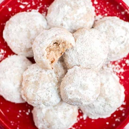 cropped snowball cookies on a red plate with a bite taken out of one of the cookies