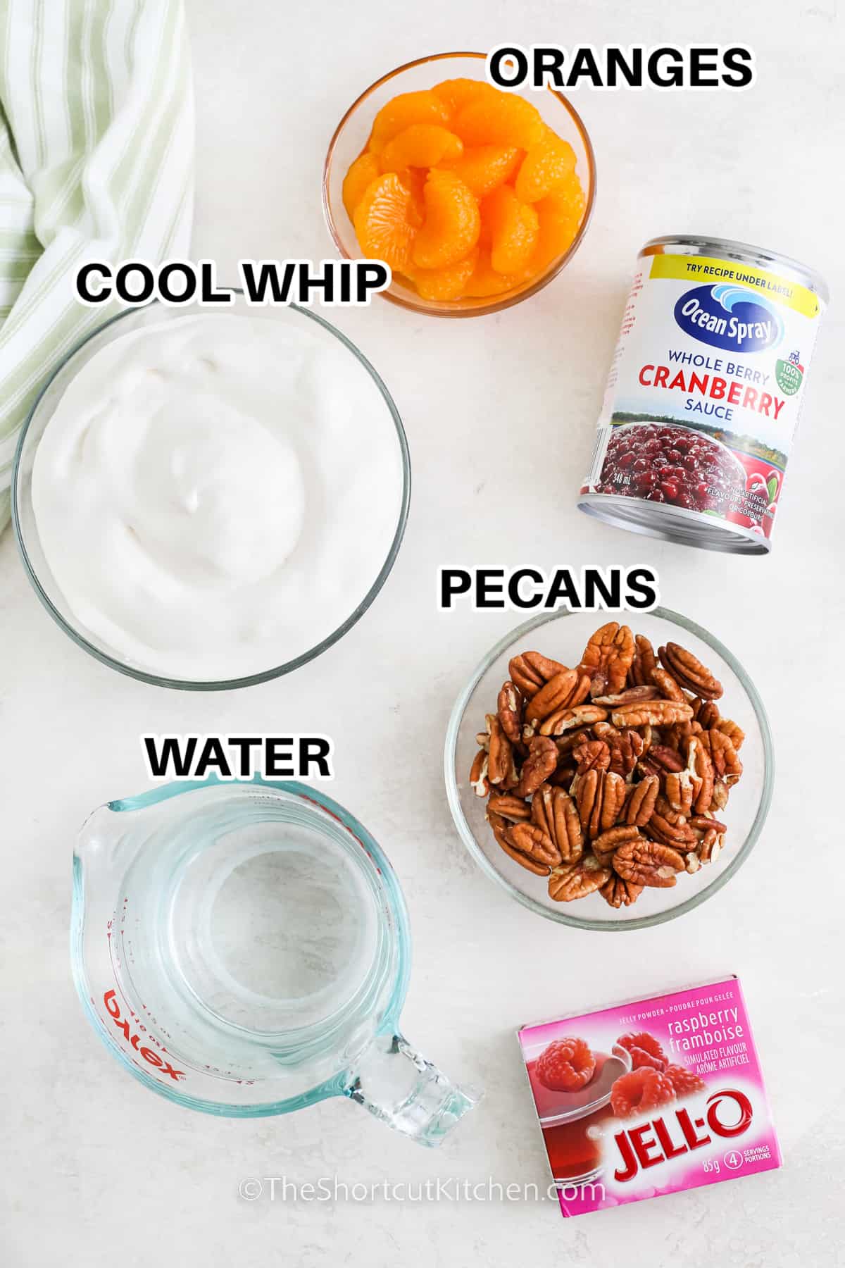 ingredients to make cranberry jello salad including oranges, cool whip, cranberry sauce, pecans, water, and jello