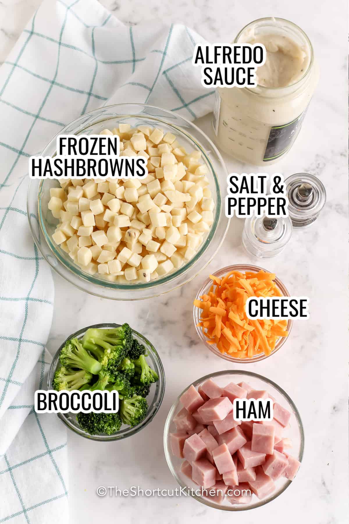 ingredients assembled to make ham and potato casserole, including frozen hashbrowns, cheese, broccoli, ham, and alfredo sauce