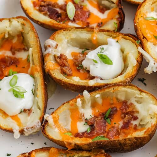Loaded potato skins on a serving dish topped with sour cream and green onions