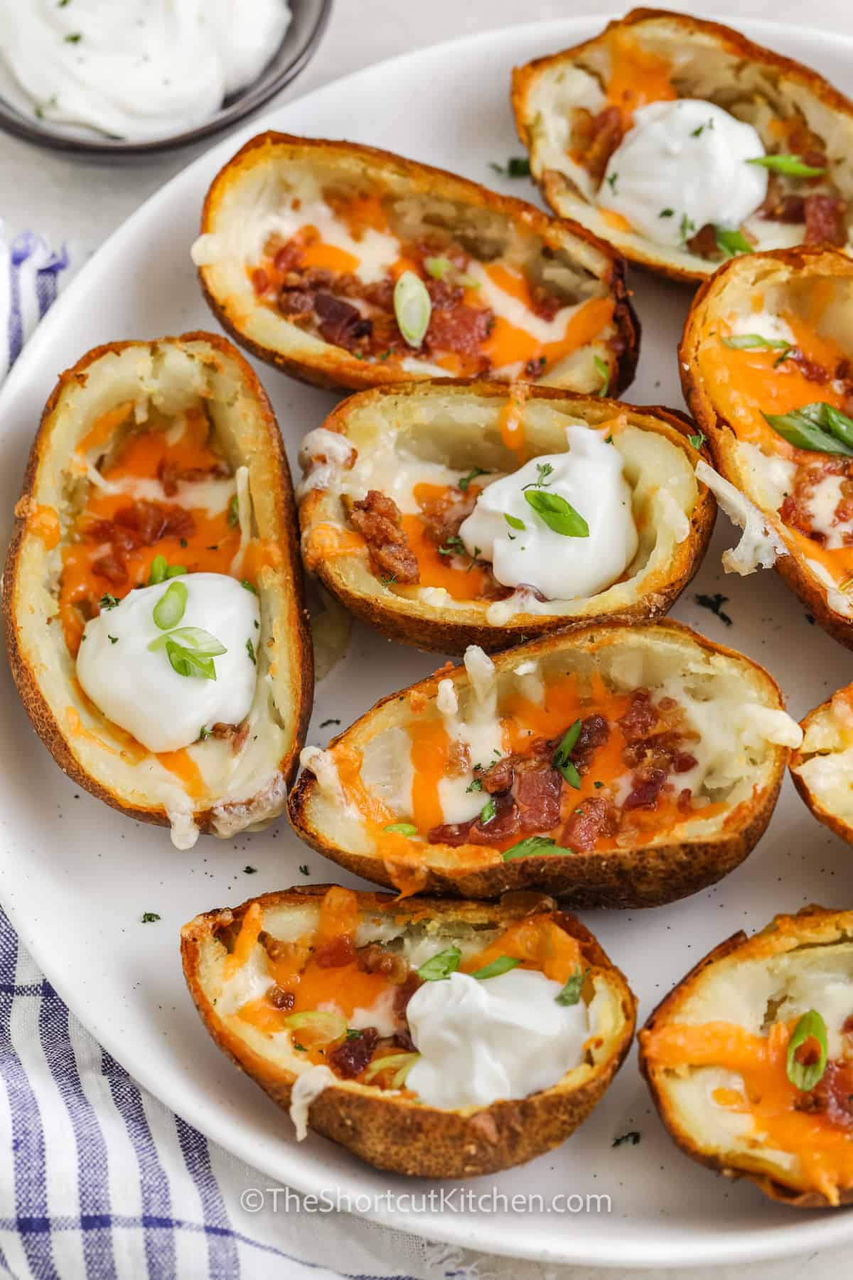 loaded potato skins topped with sour cream and green onions on a serving plate