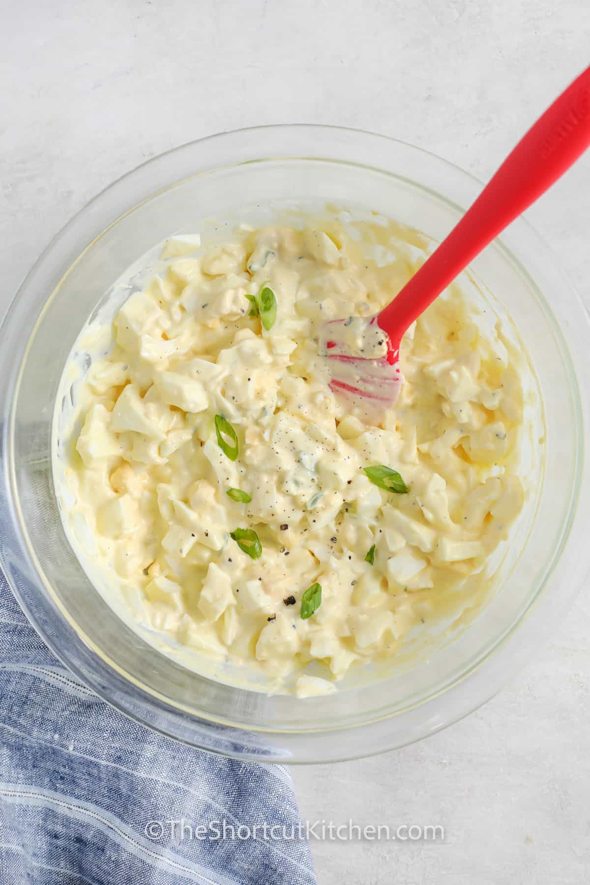 the best egg salad recipe in a small clear bowl, and garnished with sliced green onion
