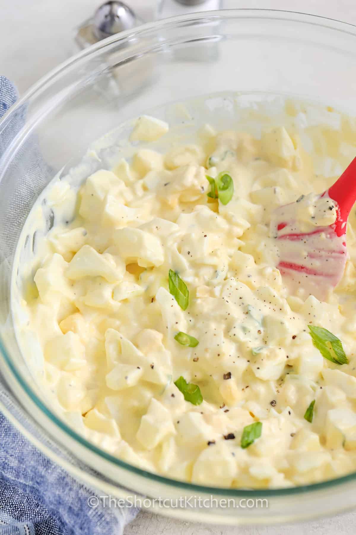 the best egg salad recipe in a clear mixing bowl, and garnished with sliced green onion