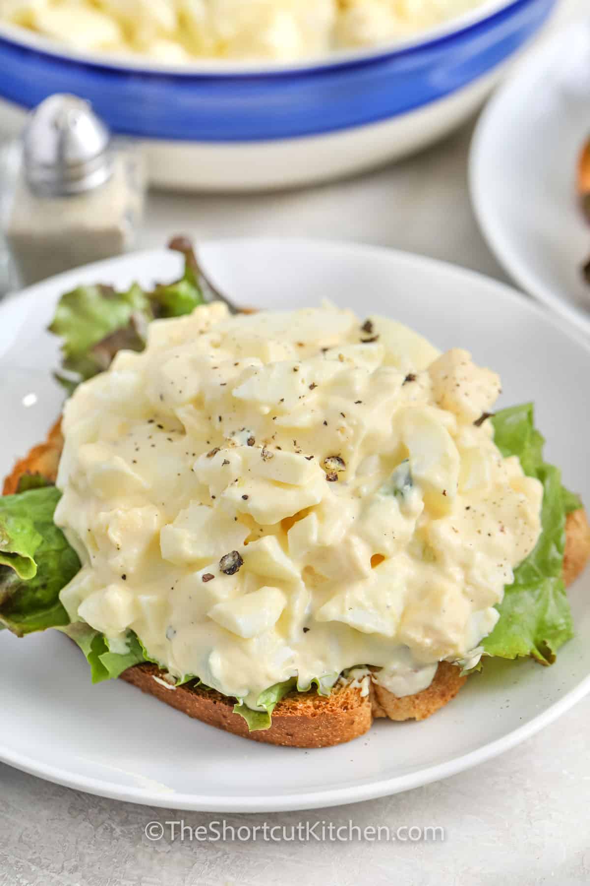 best egg salad recipe on a white plate, over leaf lettuce and a slice of bread