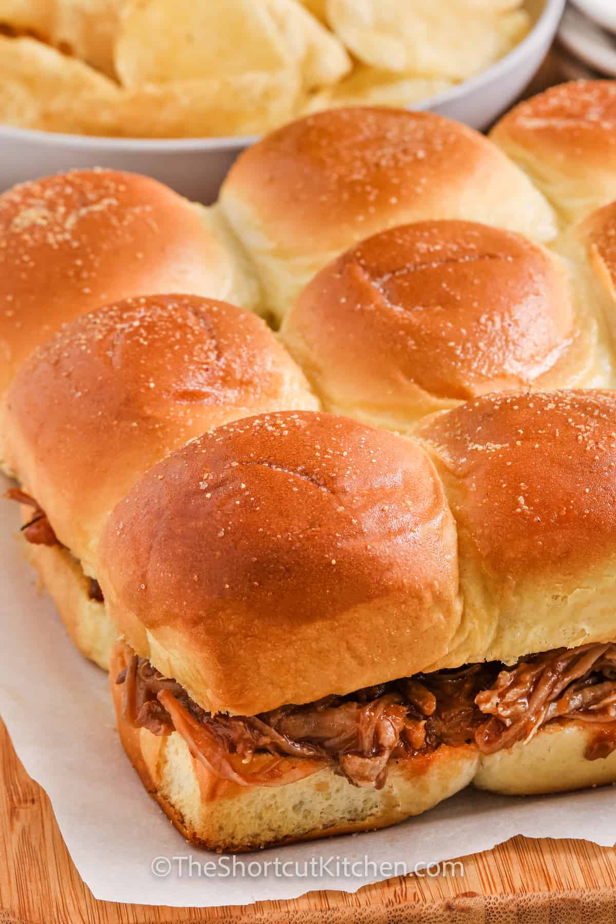 Pulled Pork Sliders on a cutting board with a bowl of chips