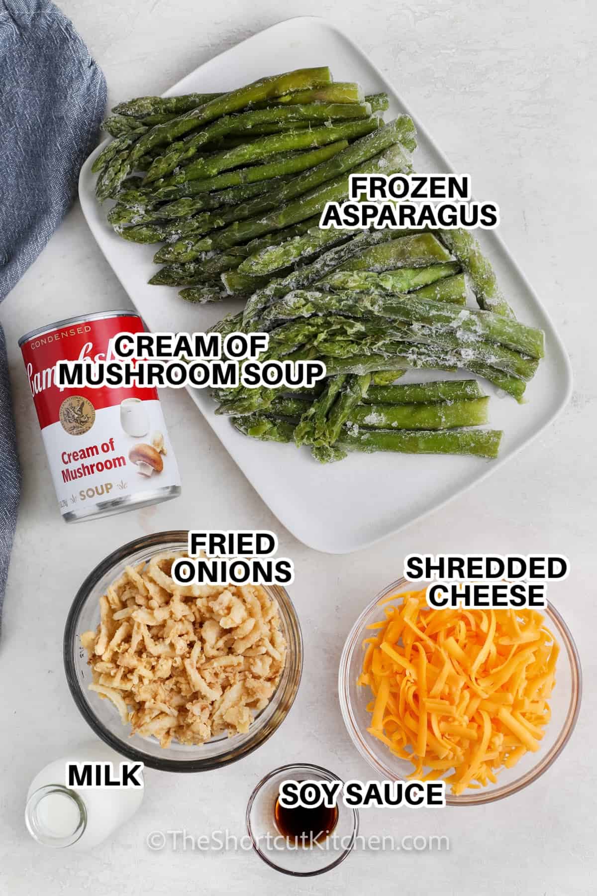 Ingredients to make Asparagus Casserole labeled: frozen asparagus, cream of mushroom soup, shredded cheese, fried onions, milk, and soy sauce