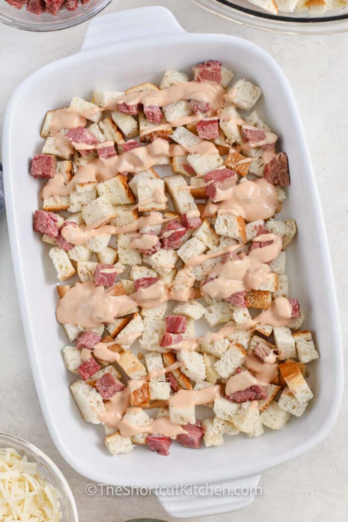 adding thousand island to bread and meat to make Reuben Casserole