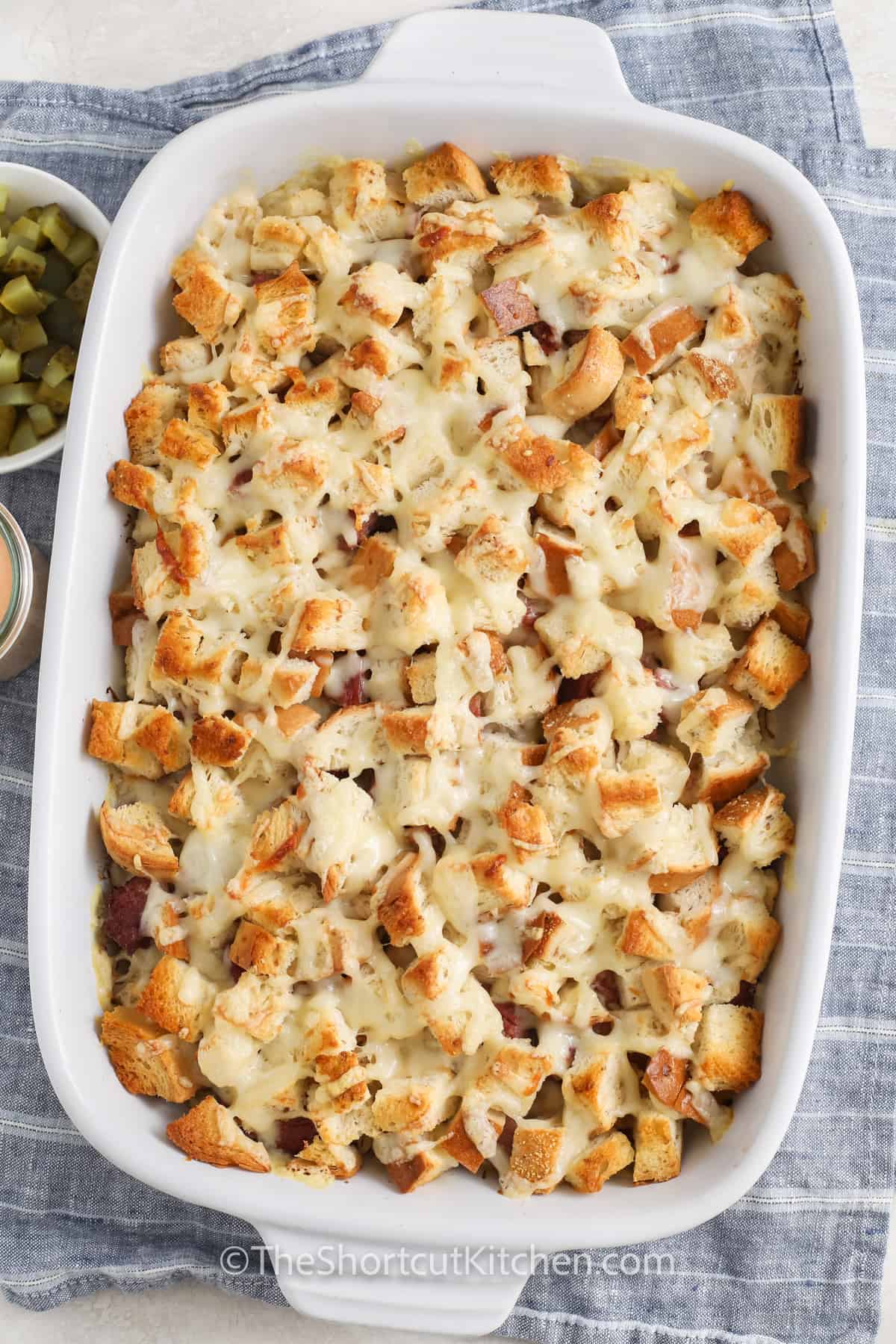 Reuben casserole turns all the classic deli flavors into one easy, baked dish. Layers of corned beef, Swiss, sauerkraut, and rye bread come together with a creamy dressing for a hands-off, crowd-pleasing dinner. Quick to assemble, perfect for weeknights, game day, or St. Patrick’s Day, and easily customized with a crispy top or extra pickles. #theshortcutkitchen baked Reuben Casserole in the dish