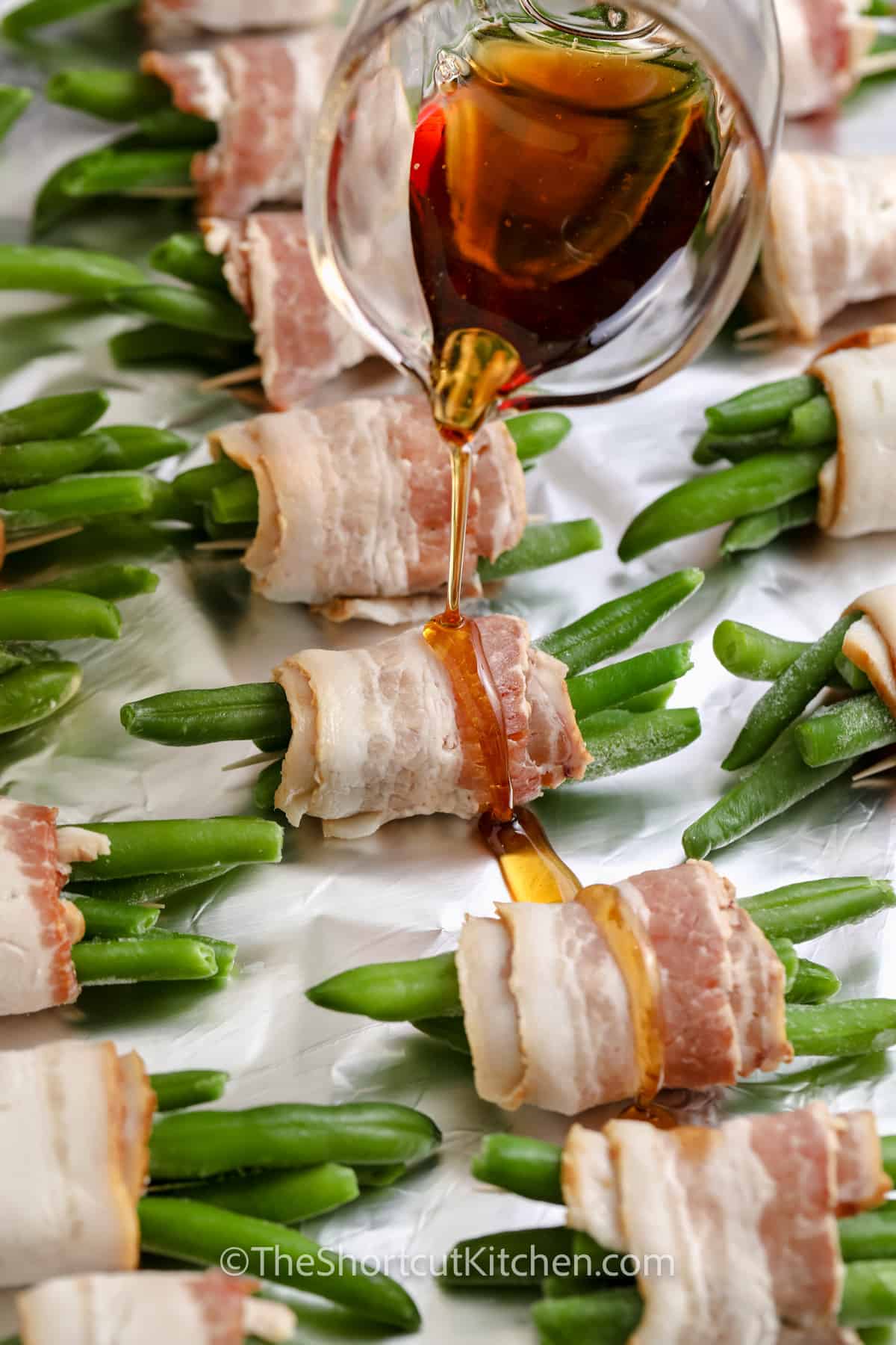 pouring maple syrup over Bacon Wrapped Green Beans
