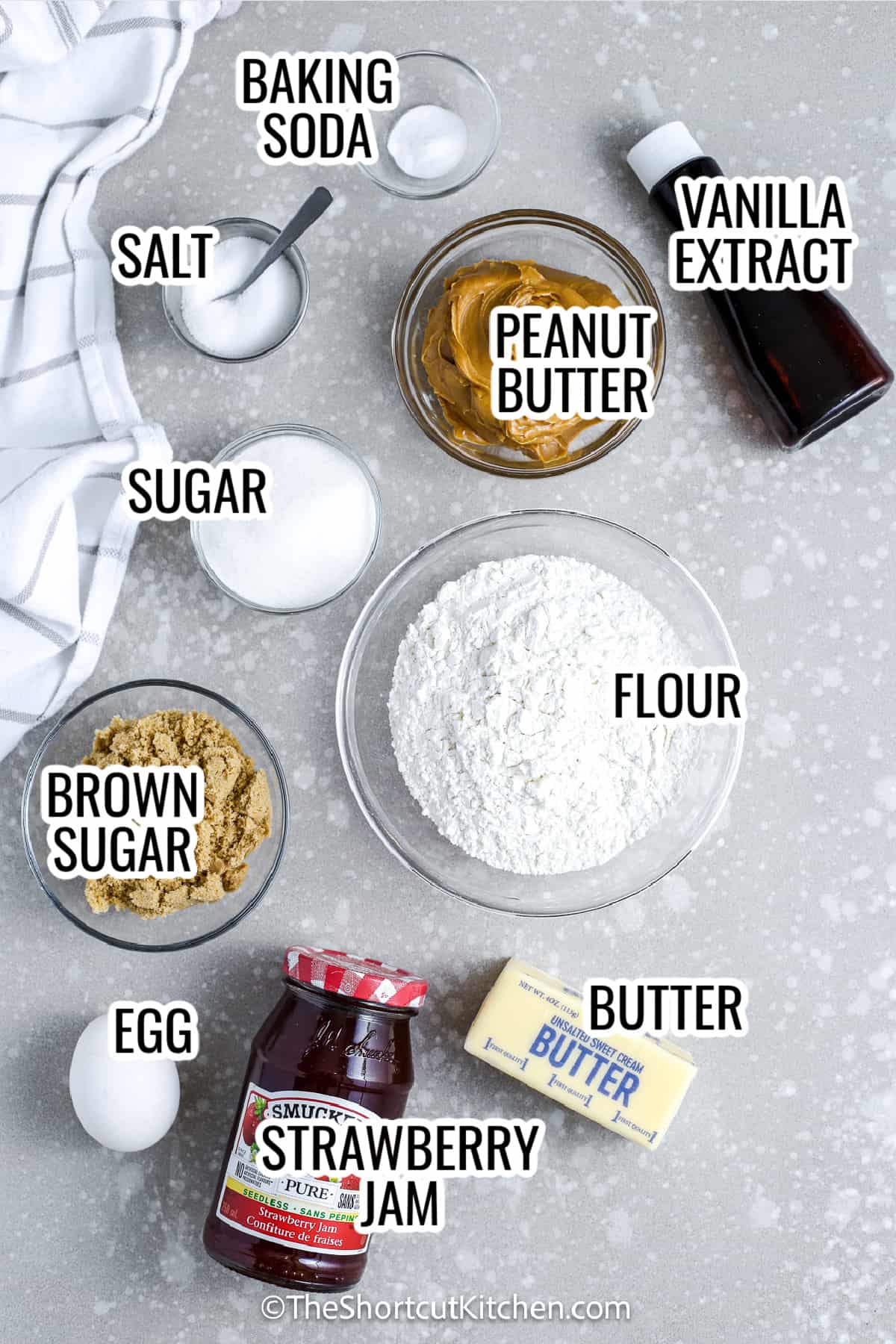 ingredients assembled to make peanut butter and jelly bars including sugar, flour, peanut butter, jam, egg, butter, baking soda, and salt