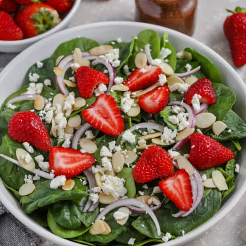 Spinach and Strawberry Salad in a white bowl with ingredients surrounding the salad.