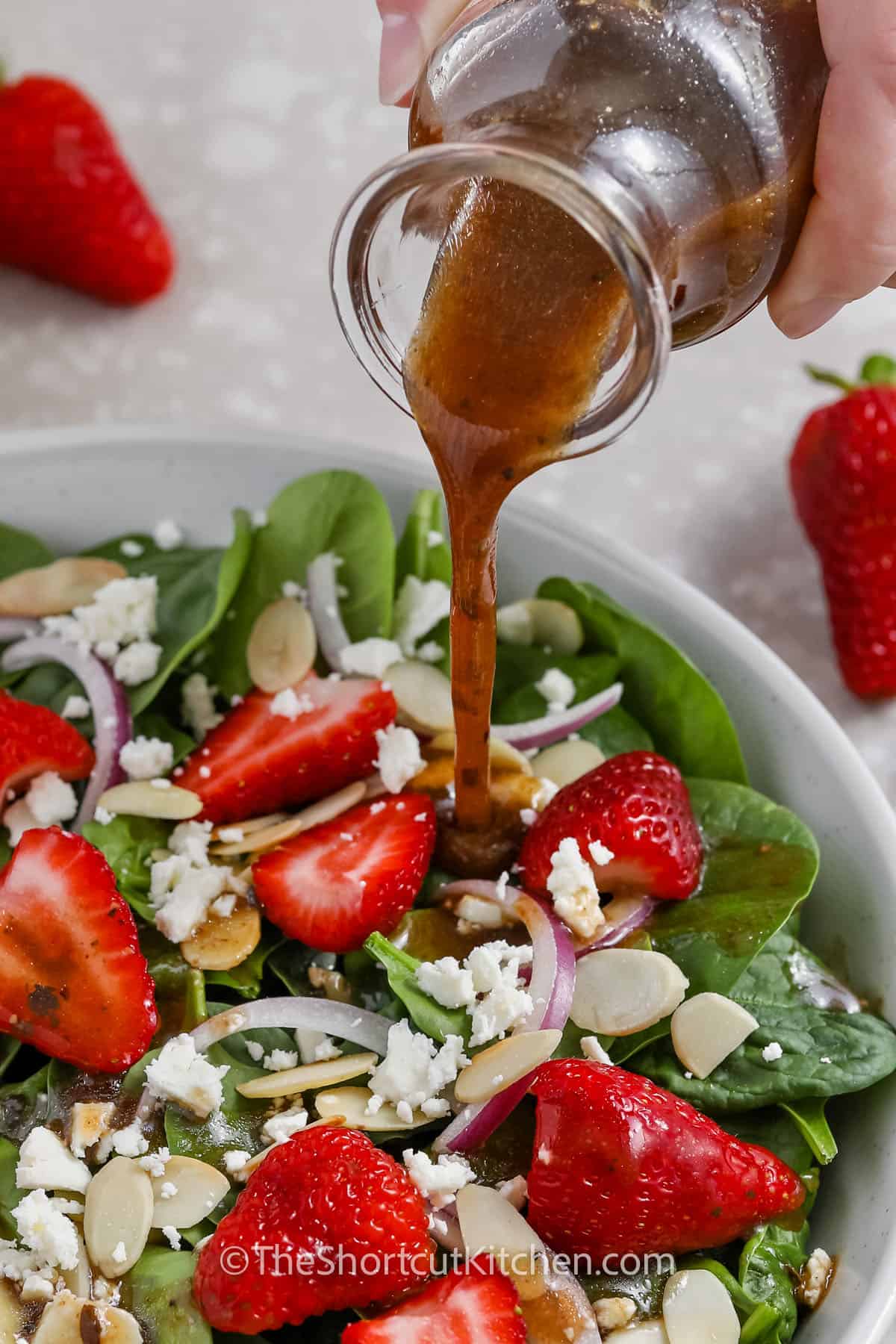 Dressing being poured onto Spinach and Strawberry Salad in a white bowl