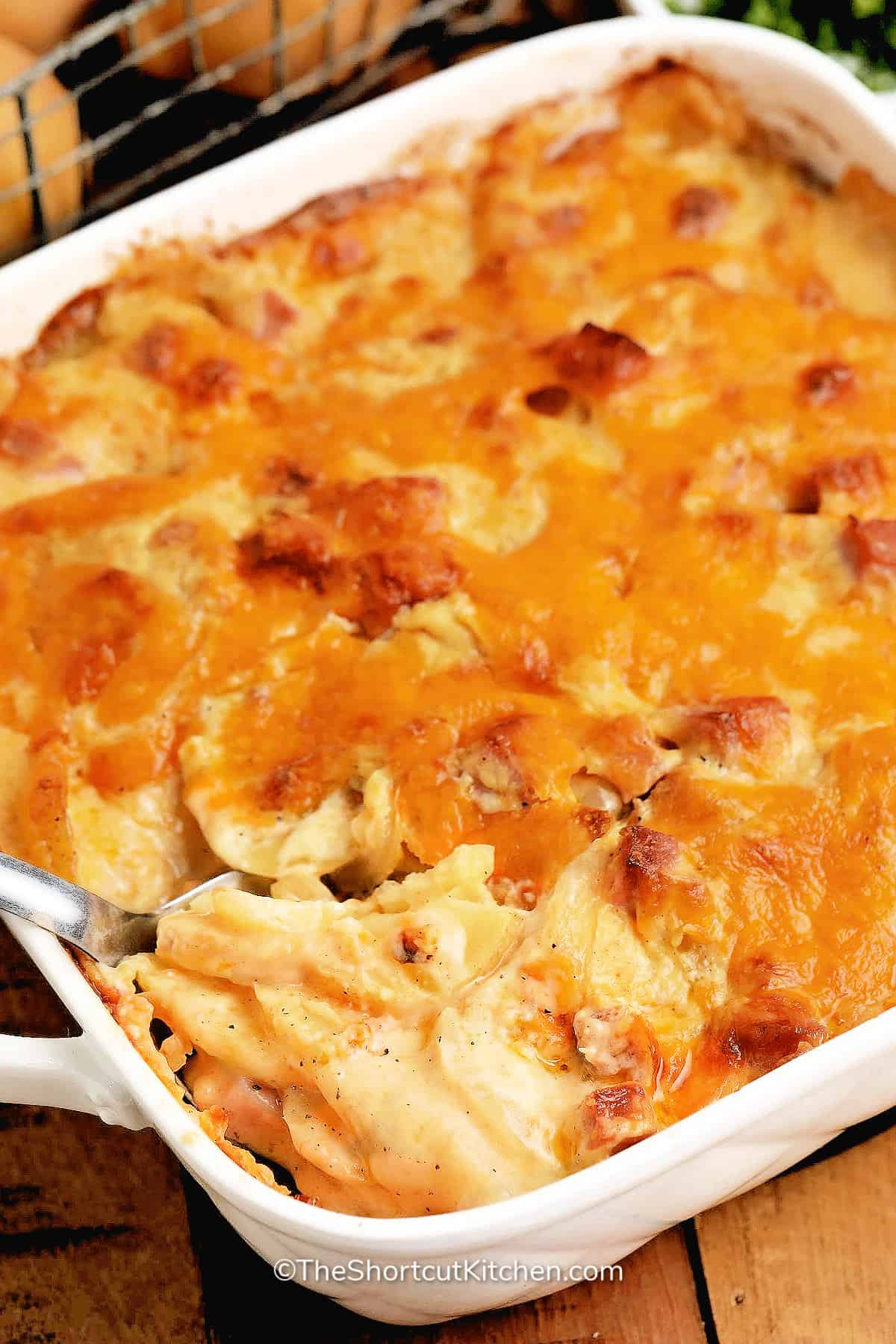 Easy Scalloped Potatoes and Ham baked in a white baking dish, with a spoon ready to lift out a serving
