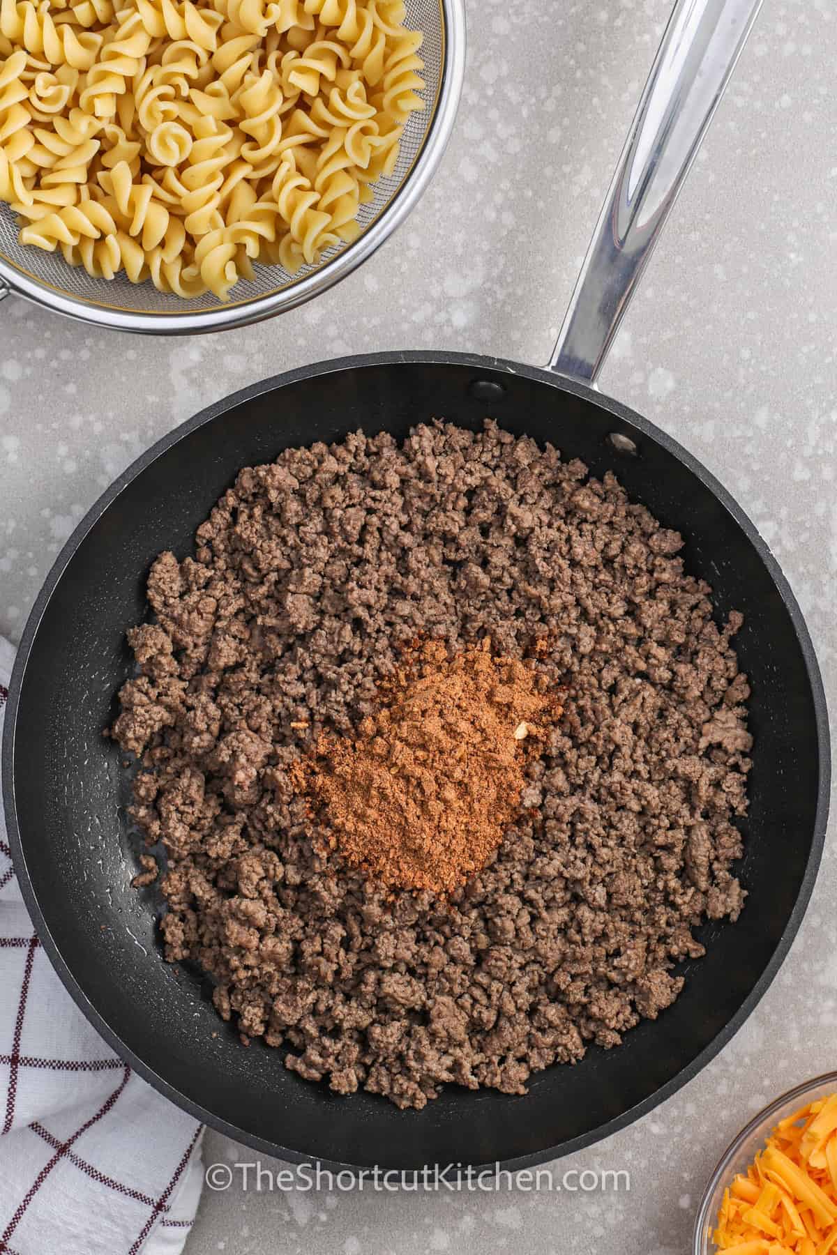 This cold taco pasta salad with ground beef is loaded with shortcut ingredients and big taco flavor. Rotini pasta, taco seasoning, shredded cheddar, cherry tomatoes, Catalina dressing, and crisp lettuce come together in a colorful salad that feeds a crowd. Keep the chips separate until serving so every bite has fresh crunch and creamy tangy dressing. Serve it at the next potluck, or for a quick dinner. #theshortcutkitchen adding taco seasoning to beef to make Taco Pasta Salad