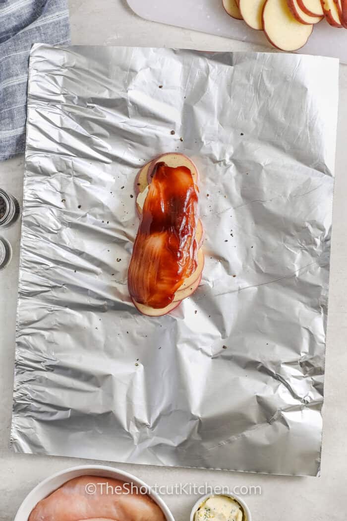 adding bbq sauce and chicken to foil to make Chicken Foil Packets