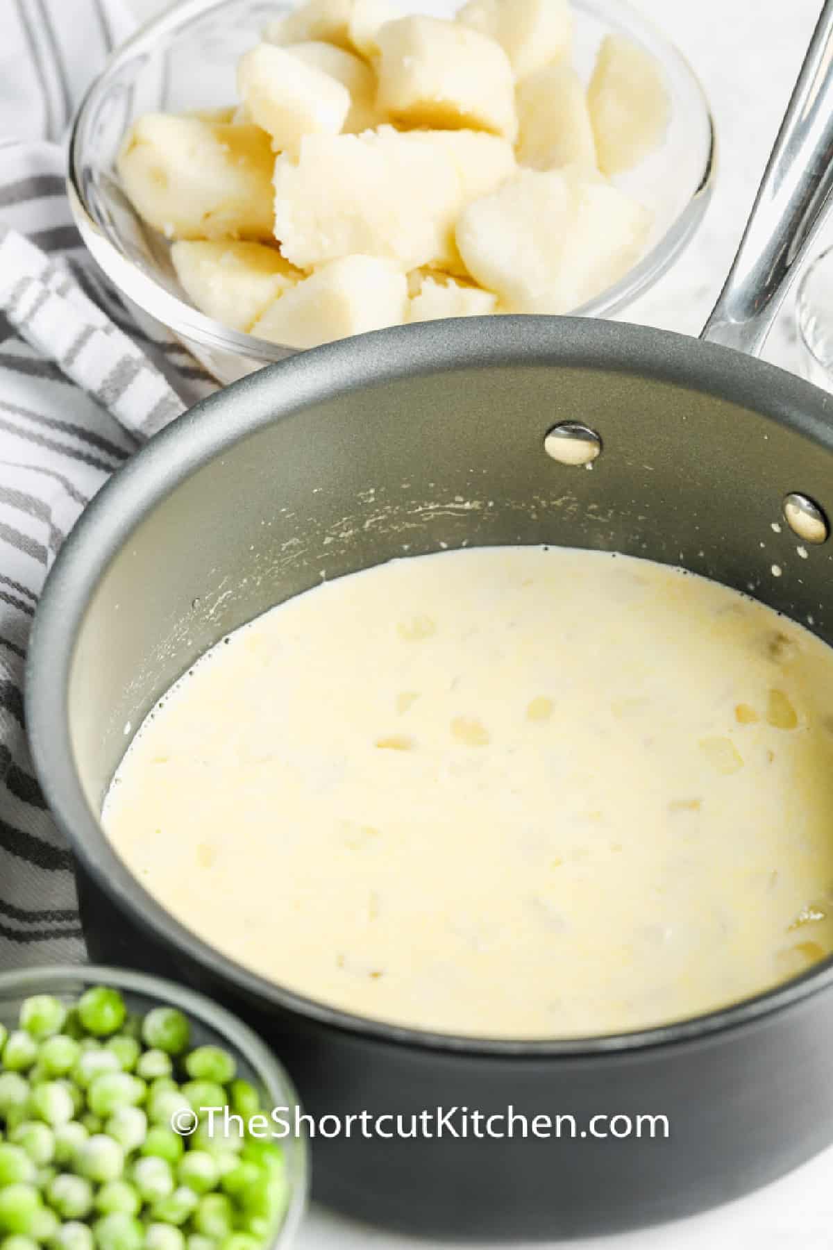 a pot of creamy sauce with potatoes and peas on the side