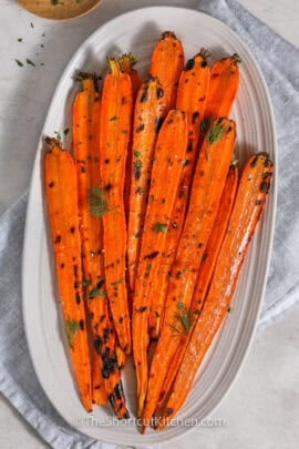 grilled carrots on a serving plate topped with fresh herbs