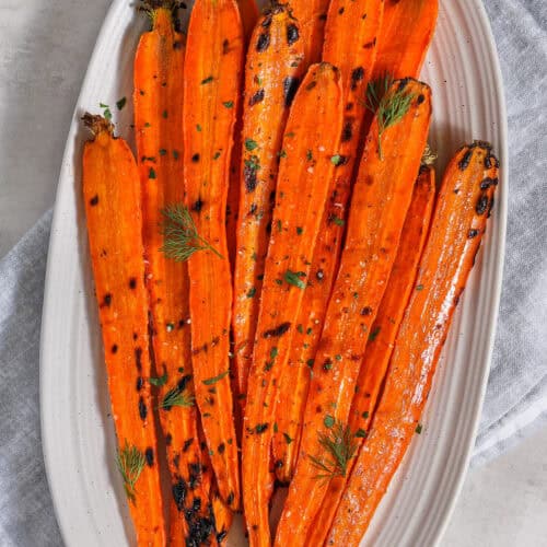 grilled carrots on a serving plate topped with fresh herbs