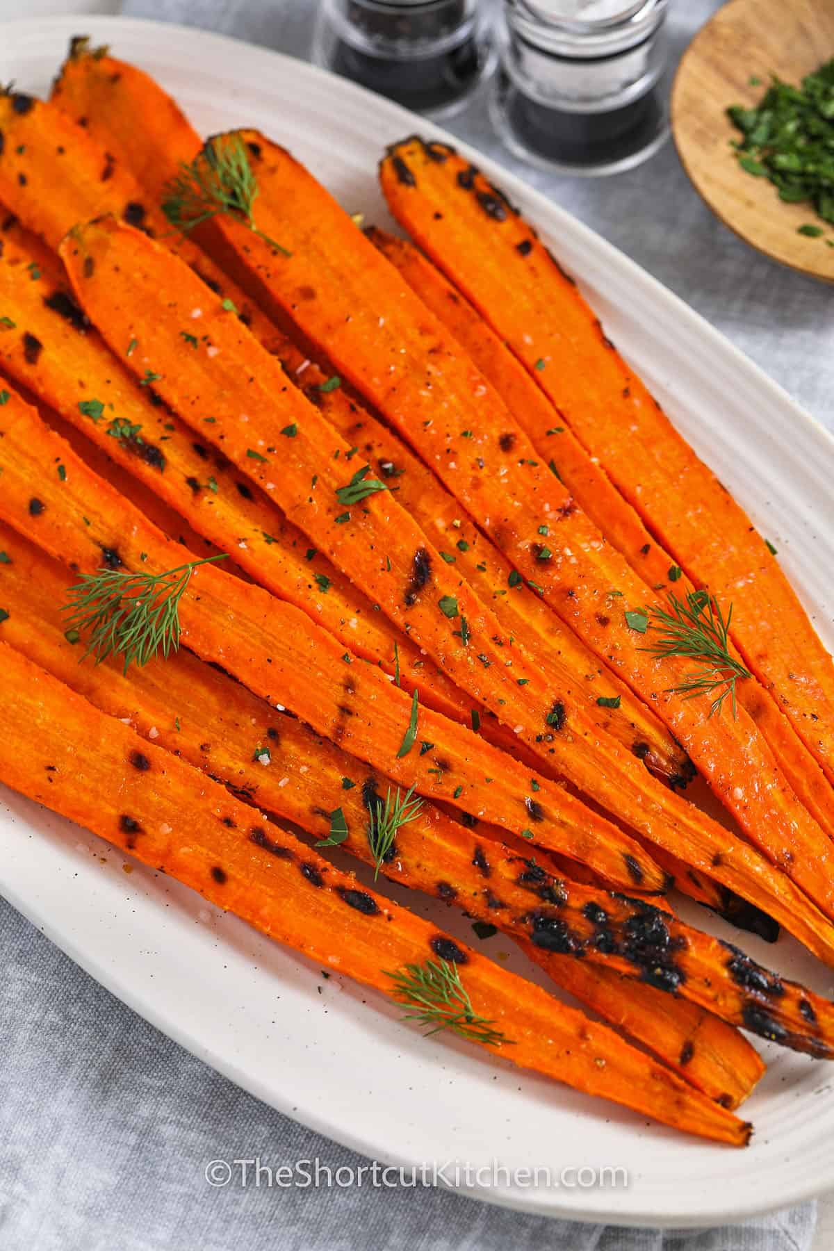 This grilled carrots recipe turns fresh carrots into a smoky, savory side dish with caramelized edges and tender centers. Made with olive oil, garlic powder, salt, and optional fresh herbs, these easy grilled carrots are perfect for BBQ menus, holiday meals, or simple family dinners. If you are looking for a grilled carrot recipe that is budget-friendly and easy to make, this one checks every box. #theshortcutkitchen A serving plate with grilled carrots