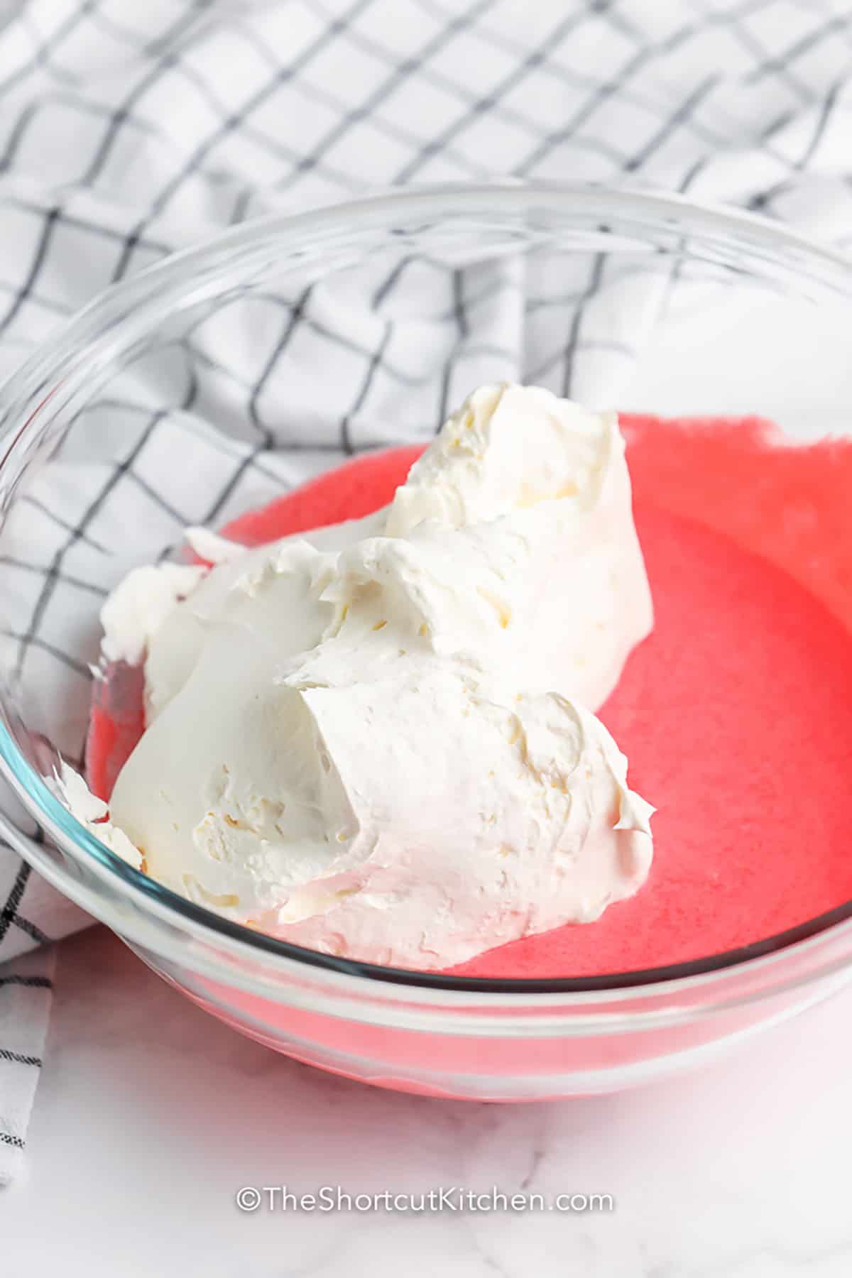 If you need a quick no-bake dessert, strawberry fluff is an easy choice with strawberry Jello, yogurt, whipped topping, and fresh strawberries. This strawberry fluff salad is sweet, airy, and soft with little marshmallow bites in every spoonful. It is a great chilled recipe for warm weather gatherings, family dinners, and potluck menus when you want something easy but crowd-pleasing. #theshortcutkitchen adding ingredients together to make Strawberry Fluff