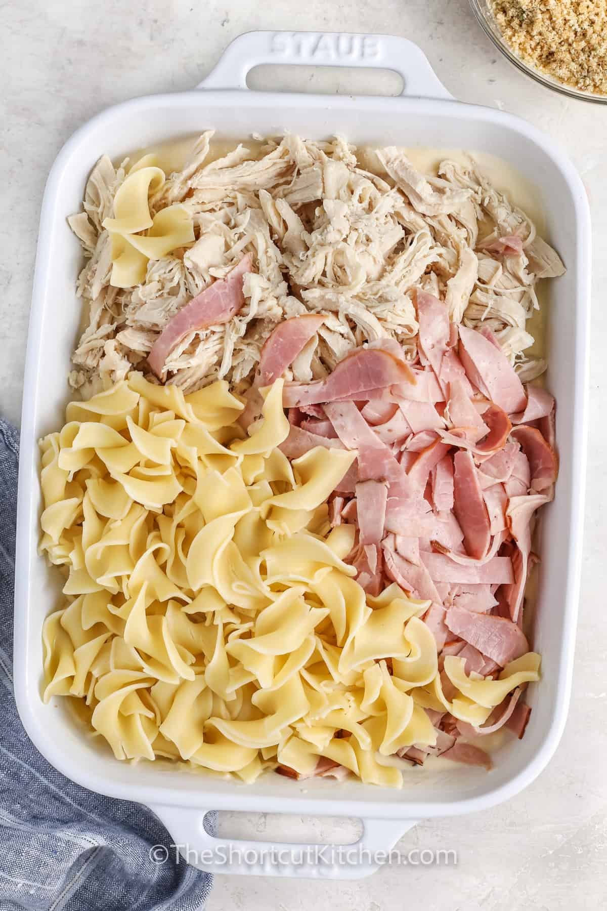 chicken cordon bleu casserole being assembled in a casserole dish