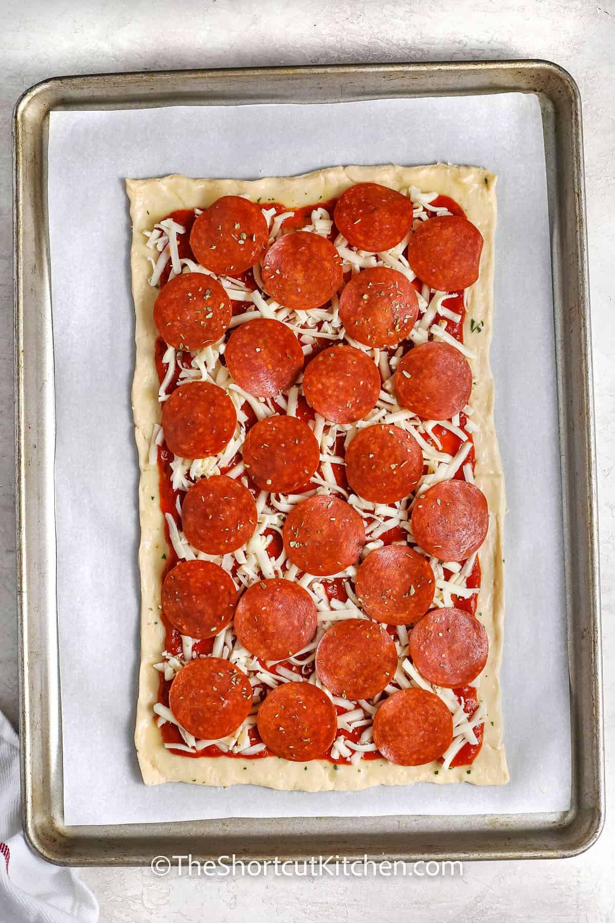 Crescent Roll Pizza is a smart pick for busy nights when dinner needs to be fast and simple. Crescent dough turns into a buttery, flaky crust with no kneading or rising, so it saves time right from the start. Spread on pizza sauce, add mozzarella and pepperoni for a classic, or set out toppings and let everyone build their own. It all bakes on one sheet pan, making prep, serving, and cleanup quick and easy. #theshortcutkitchen Crescent Roll Pizza before cooking