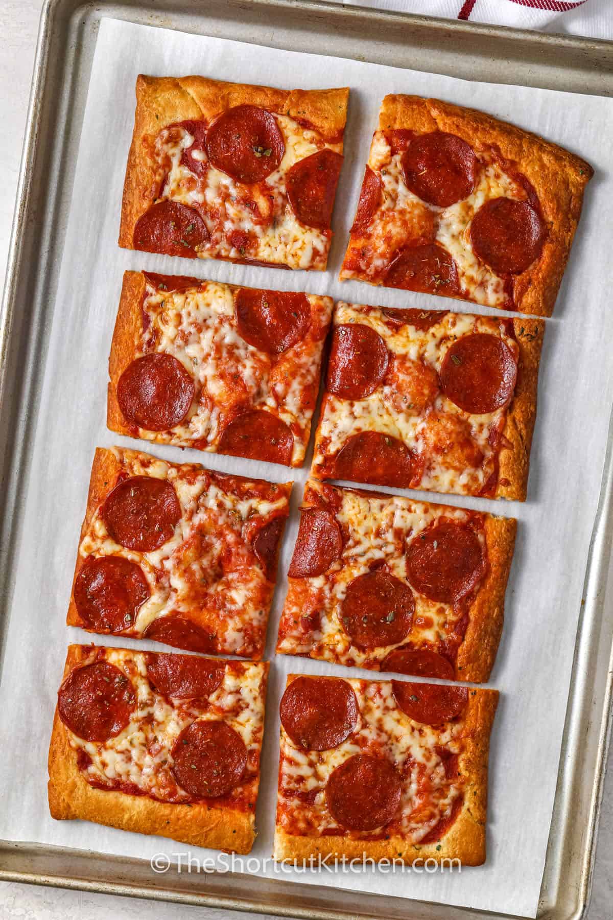 Make this quick Crescent Roll Pizza when pizza cravings hit. This pizza starts with refrigerated crescent roll dough pressed into a sheet pan, brushed with garlic butter, then topped with pizza sauce, shredded mozzarella, and pepperoni. It bakes up golden and melty in minutes. Perfect for busy weeknights, game day trays, and the leftovers make easy lunches. #theshortcutkitchen Crescent Roll Pizza cooked on a sheet pan