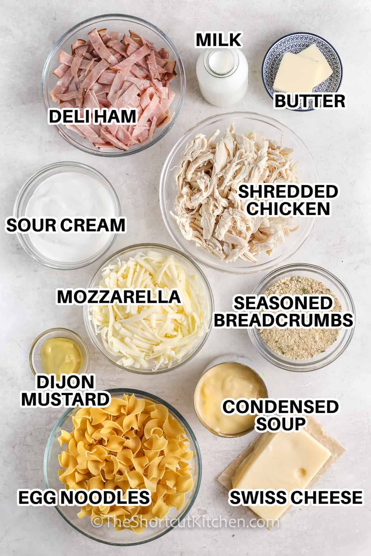 Ingredients to make chicken cordon bleu casserole labelled: milk, butter, deli ham, shredded chicken, sour cream, mozzarella, seasoned breadcrumbs, dijon mustard, condensed soup, egg noodles, and swiss cheese.