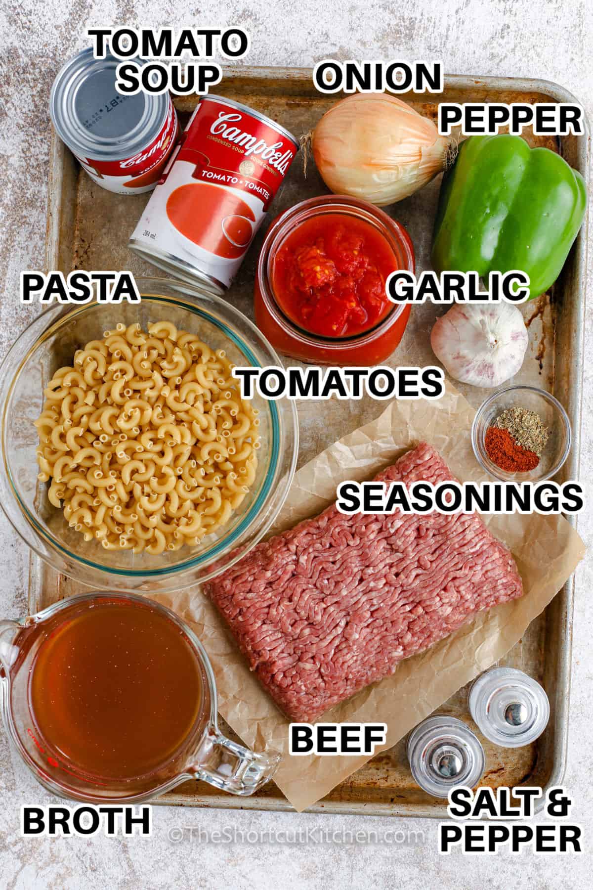 ingredients assembled to make hamburger macaroni soup including tomato soup, onion, pepper, pasta, tomatoes, seasoning, ground beef, broth, and salt and pepper