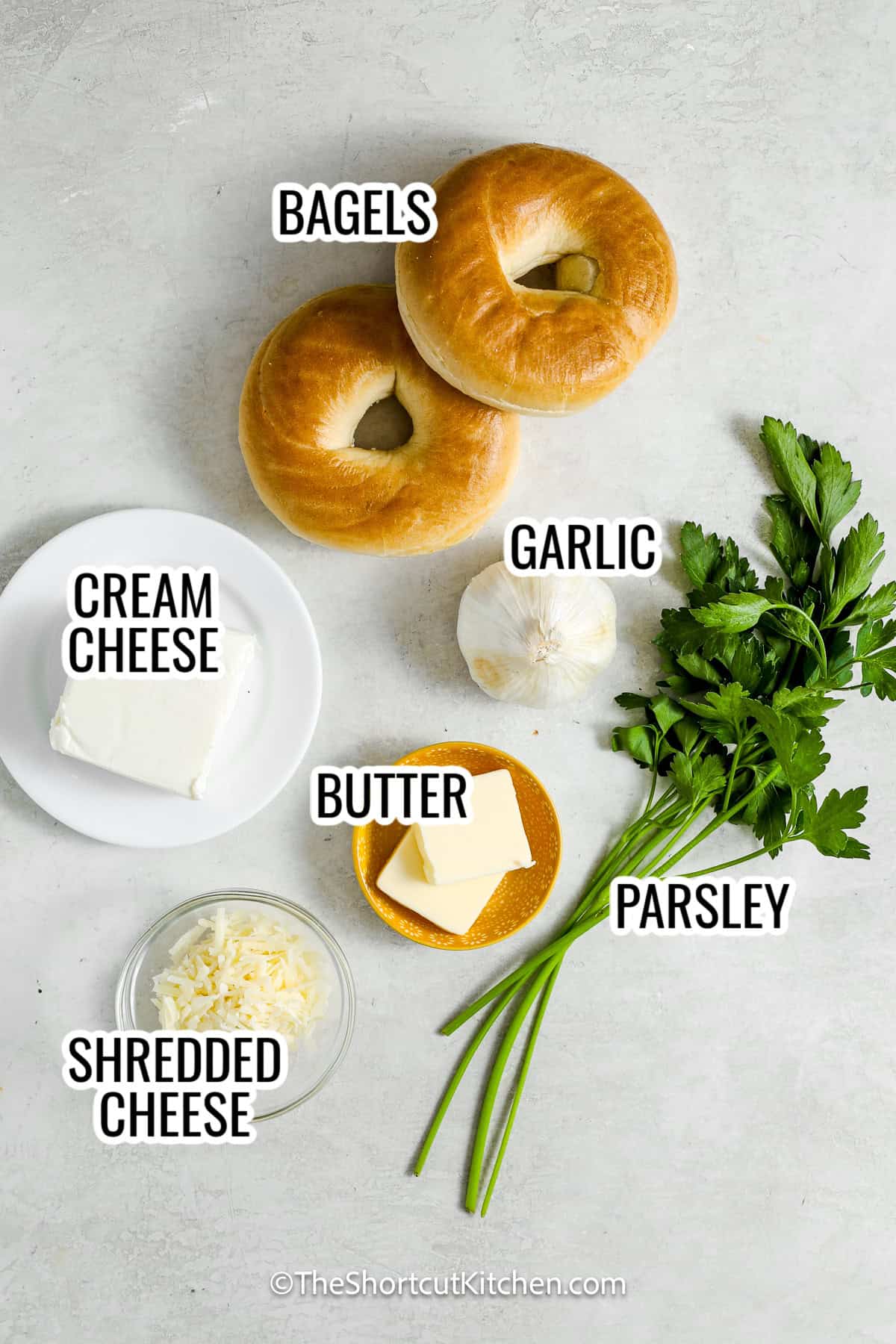 ingredients assembled to make stuffed bagels, including bagels, cream cheese, garlic, shredded cheese, butter, garlic, and parsley