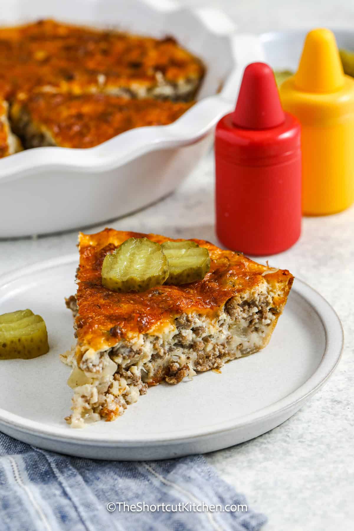 Looking for a quick ground beef dinner? This Bisquick cheeseburger pie uses Bisquick to create a golden, buttery crust over a layer of seasoned hamburger and melted cheese. It’s perfect for those nights when you need to get dinner on the table fast without sacrificing flavor. A classic comfort food recipe for any home cook. #theshortcutkitchen a slice of Bisquick Cheeseburger Pie