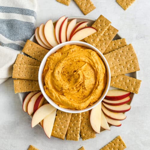 a bowl of pumpkin dip on a platter of apples and graham wafers