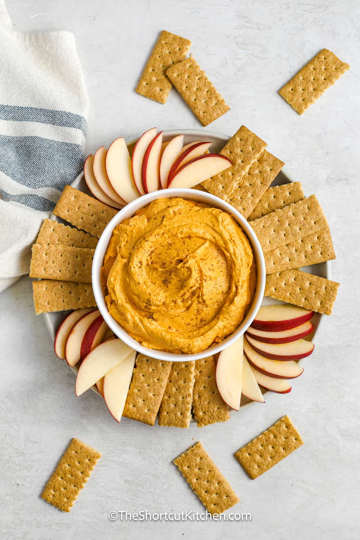 a bowl of pumpkin dip on a platter of apples and graham wafers