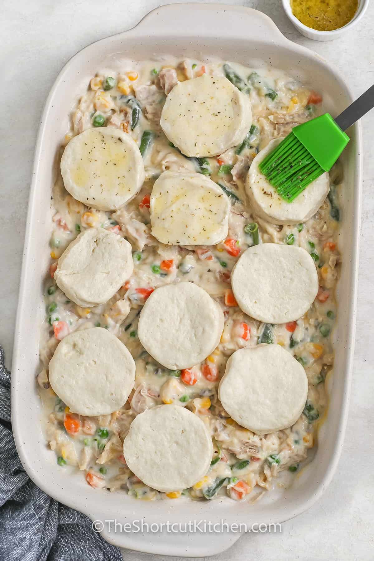 brushing garlic butter over biscuits to make Easy Chicken Pot Pie Casserole