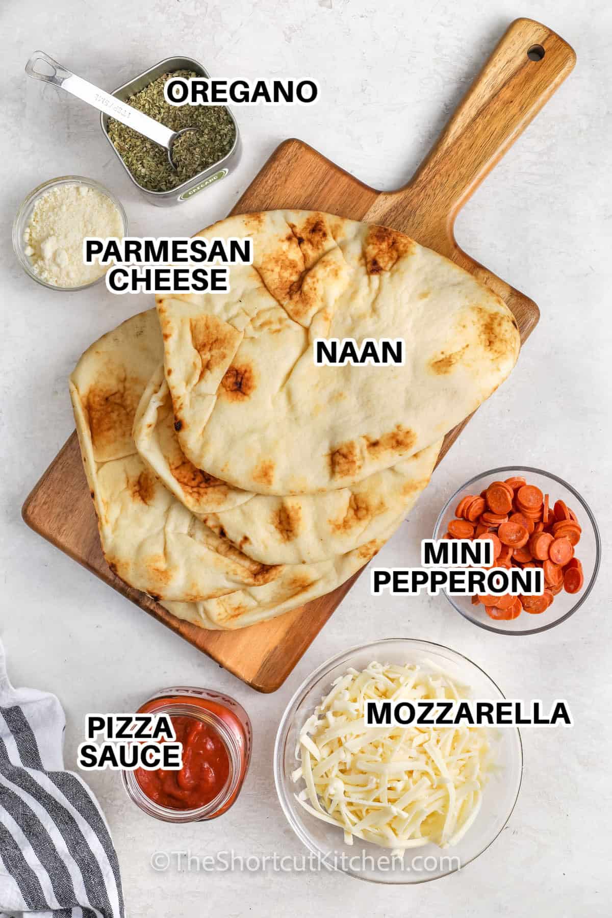 Ingredients to make naan pizza labelled: oregano, parmesan cheese, naan, mini pepperoni, mozzarella, and pizza sauce.