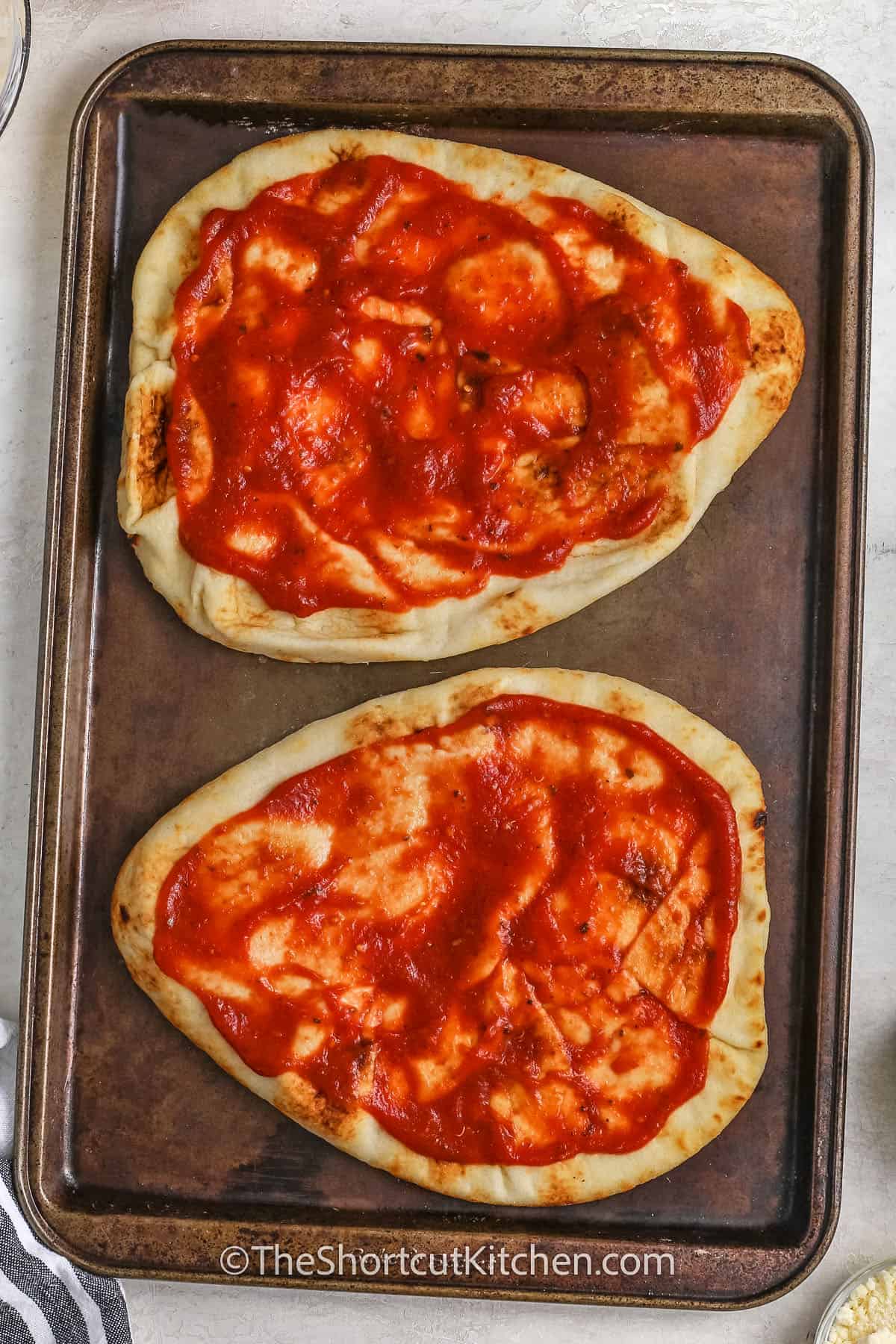 naan topped with pizza sauce on a baking tray