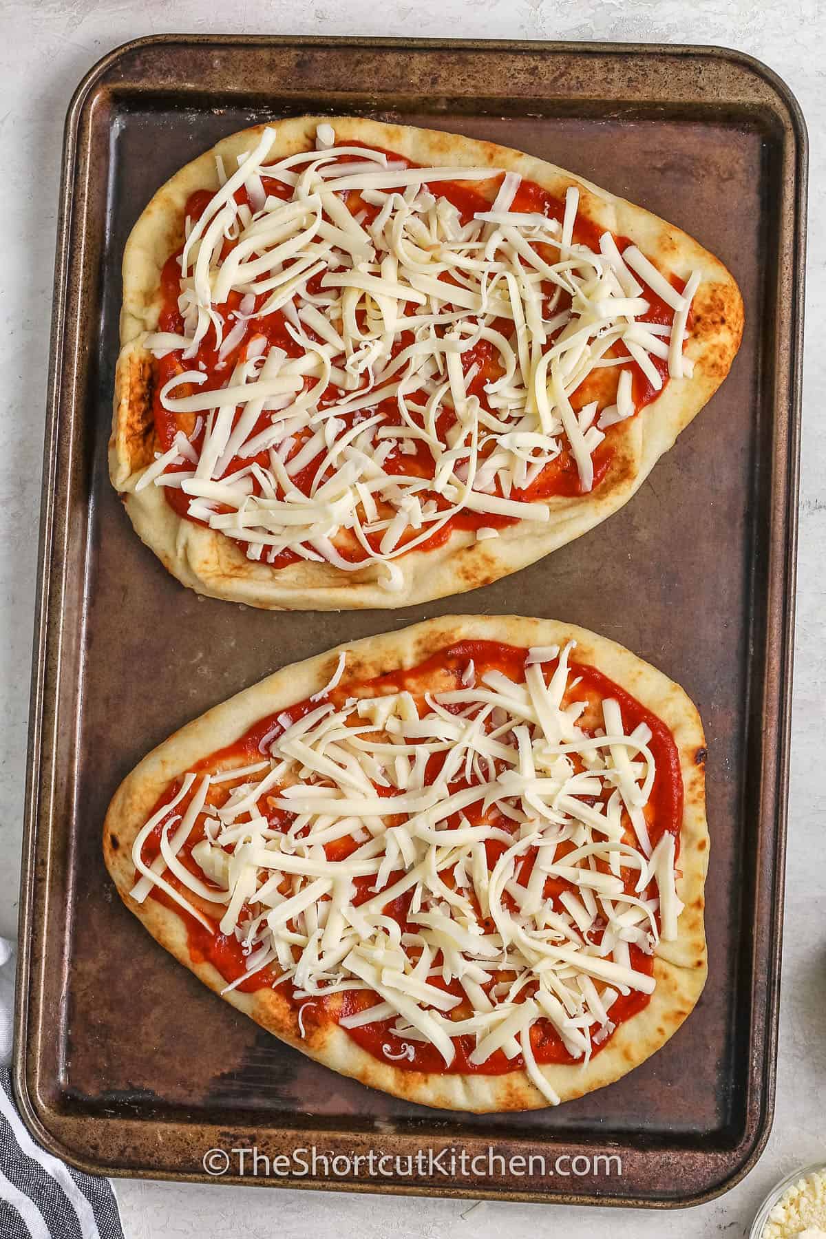 Naan topped with pizza sauce and cheese on a baking tray