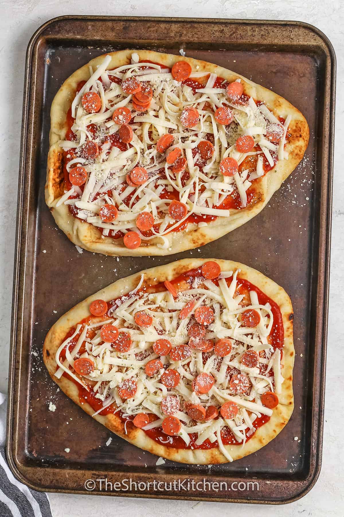 naan pizza topped with pizza sauce, cheese and mini pepperoni on a baking tray