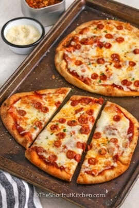 baked naan pizzas sliced on a baking tray