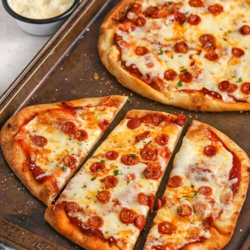 baked naan pizzas sliced on a baking tray