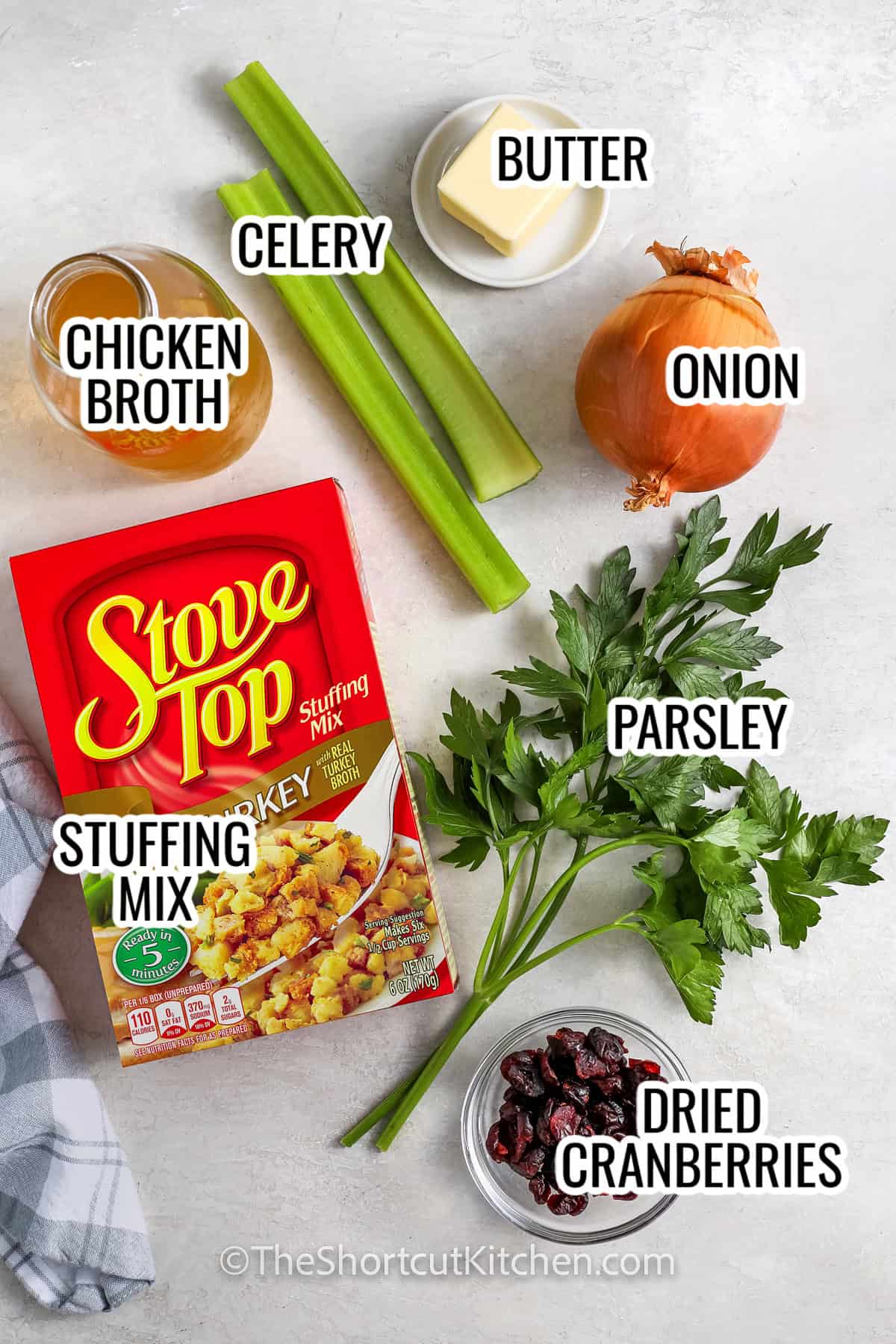 ingredients assembled to make thanksgiving stuffing including chicken broth, stuffing mix, celery, onion, butter, and dried cranberrie