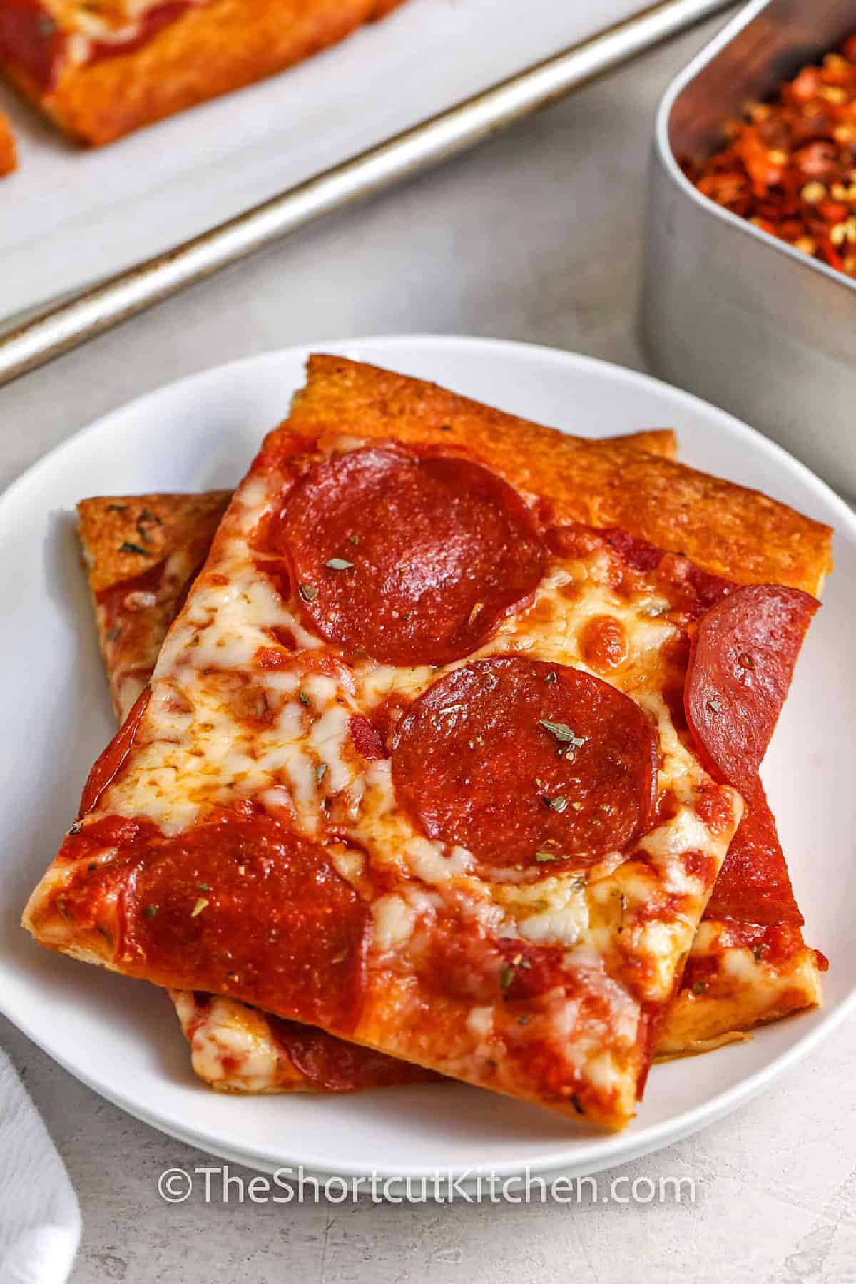 Crescent Roll Pizza is the easiest shortcut pizza night. Crescent roll dough bakes into a flaky, buttery crust, then gets brushed with garlic butter, topped with pizza sauce, mozzarella, and pepperoni. This crescent roll pizza recipe is made on a sheet pan for quick prep and easy cleanup. Swap toppings, keep it kid-friendly, and slice into squares for dinner or a party snack. #theshortcutkitchen close up of Crescent Roll Pizza on a plate