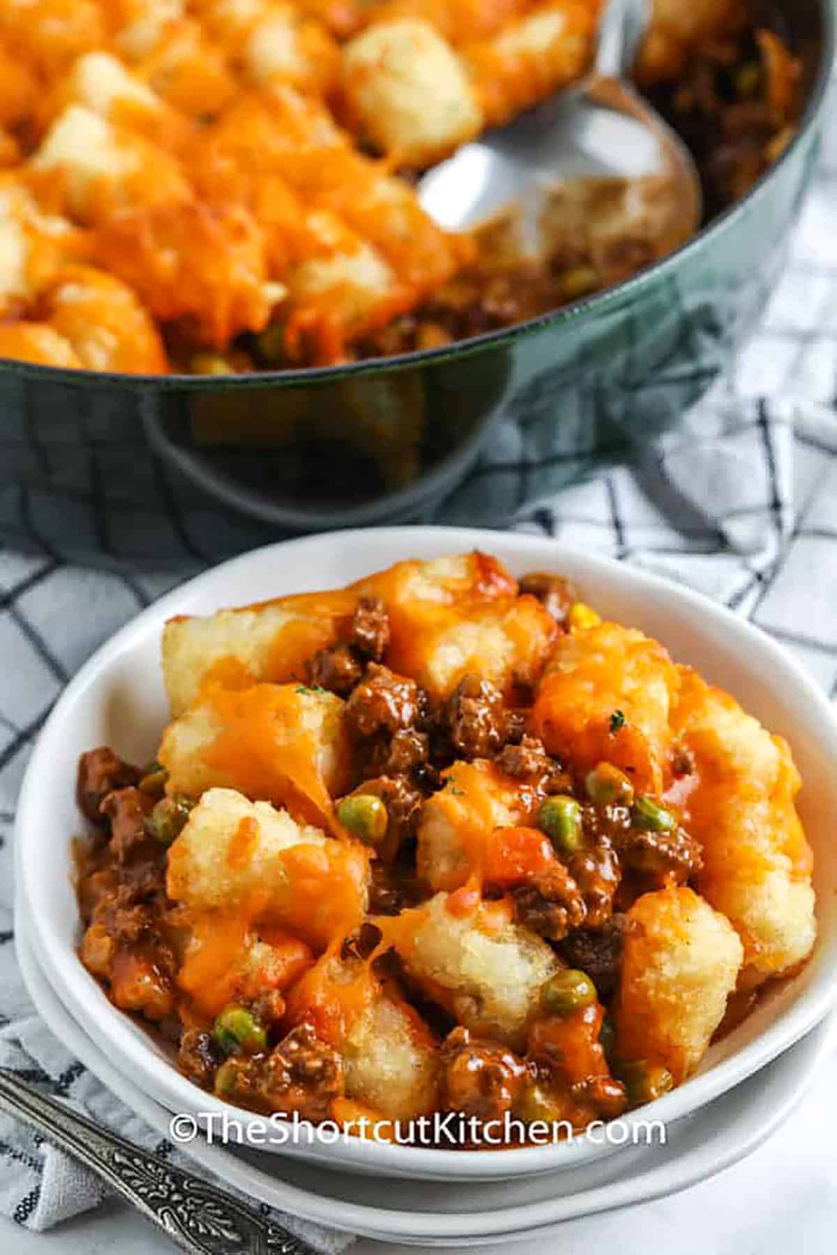 Nothing beats an easy shepherd’s pie recipe for a warm and comforting meal. Ground beef and onions are simmered with seasonings, tomato soup and frozen vegetables, creating a rich and flavorful filling. Topped with crispy tater tots and gooey melted cheese, this dish comes together quickly. No need to mash potatoes or carrots. Just layer and bake for the best weeknight dinner. It’s a simple, delicious way to enjoy a classic dish with a fun twist! #theshortcutkitchen shepherd's pie in a white bowl