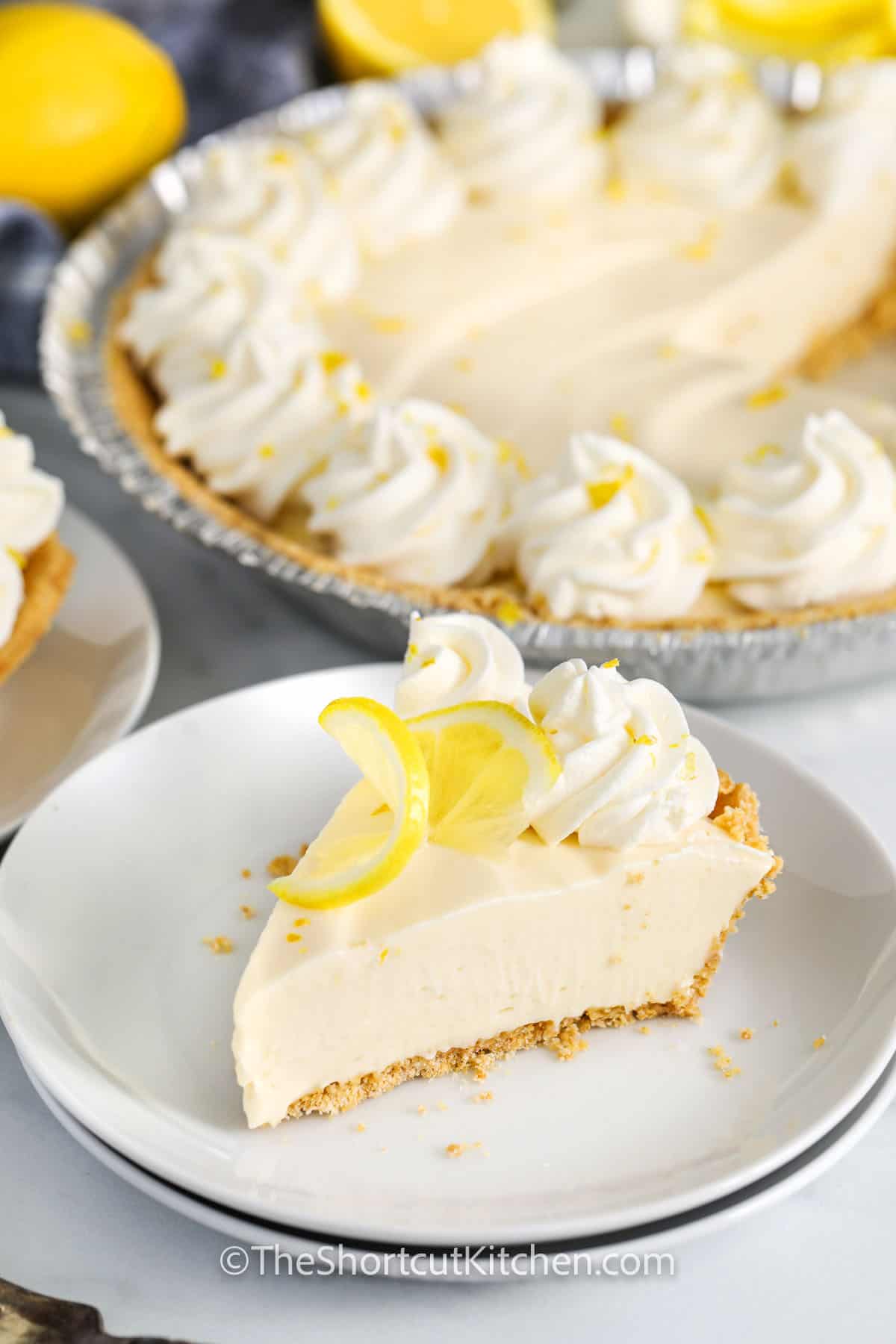 This no-bake creamy lemon pie recipe is a quick and easy summer dessert with just four simple ingredients. Cream cheese, lemon juice, and sweetened condensed milk blend into a smooth, creamy filling, which gets spread into a graham cracker crust. Chill until set, and you've got a bright, lemony treat perfect for warm days. Serve it as is or with fluffy whipped topping and fresh lemon slices for extra charm. #theshortcutkitchen slice of Creamy Lemon Pie Recipe with piece in the back