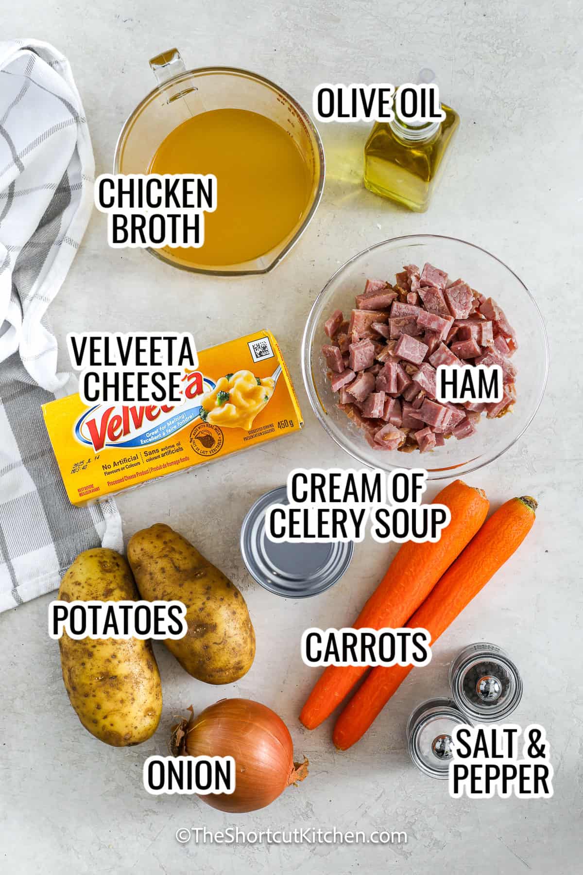 ingredients assembled to make cheesy ham and potato soup, including chicken broth, ham, olive oil, velveeta cheese, potatoes, carrots, cream of celery soup, and onion