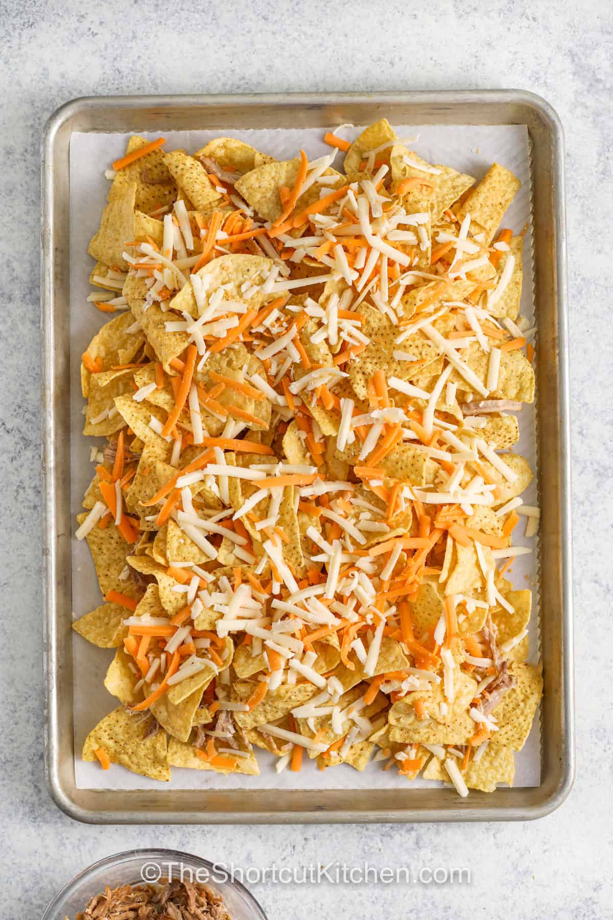 adding another layer of chips and cheese to sheet pan to make Carnitas Nachos