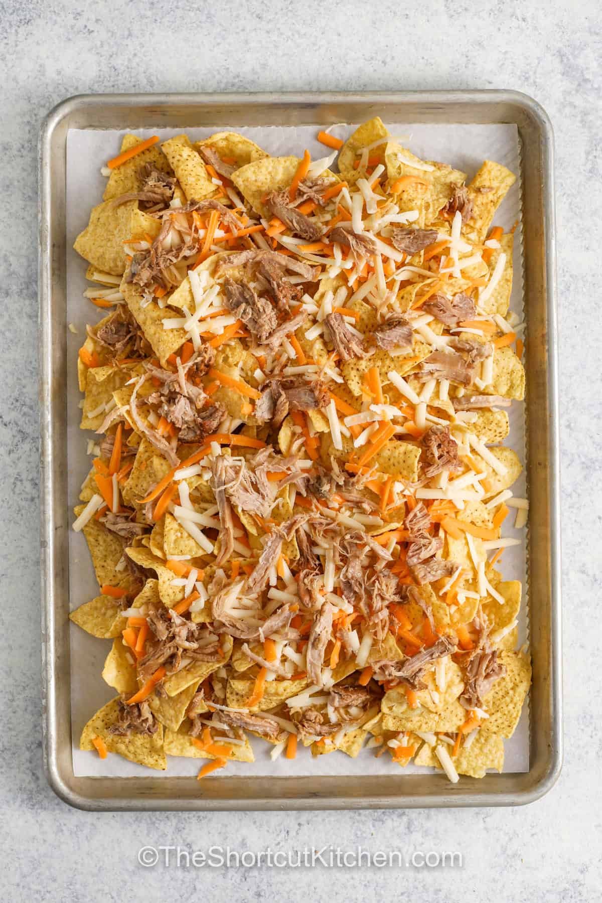 adding meat and cheese to chips to make Carnitas Nachos