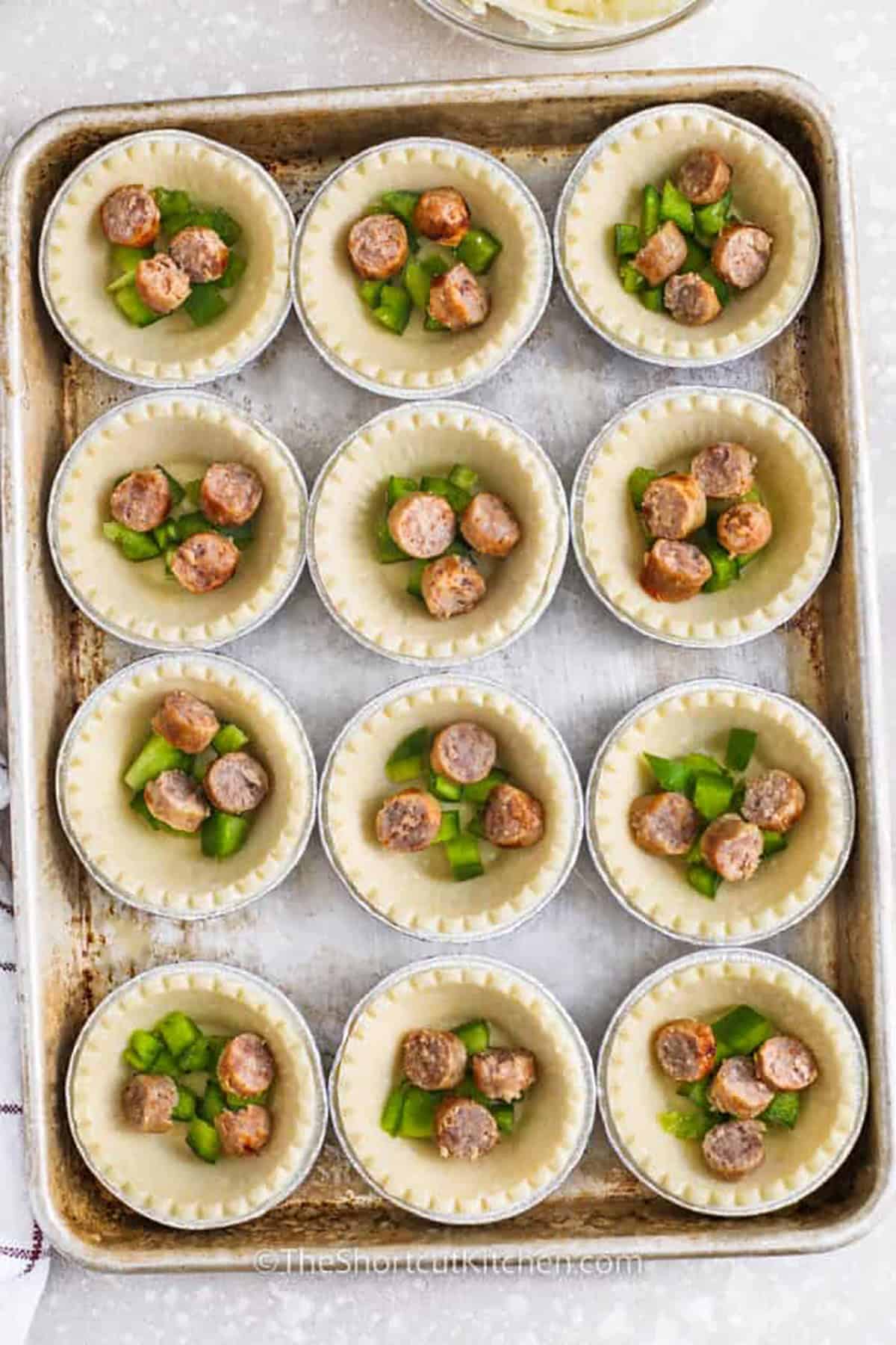adding pepper and sausage to tart shells to make Mini Quiches